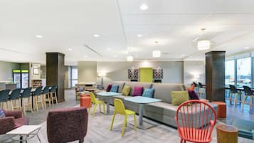 A modern lounge area with a sofa, chairs, tables, and a bar area.