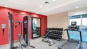 A gym with a red wall, a mirror, a bench, dumbbells, and a treadmill.