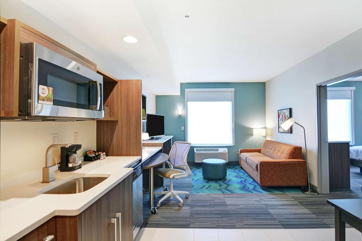Une chambre d’hôtel compacte comprenant un coin cuisine, un canapé, un bureau et une grande fenêtre.