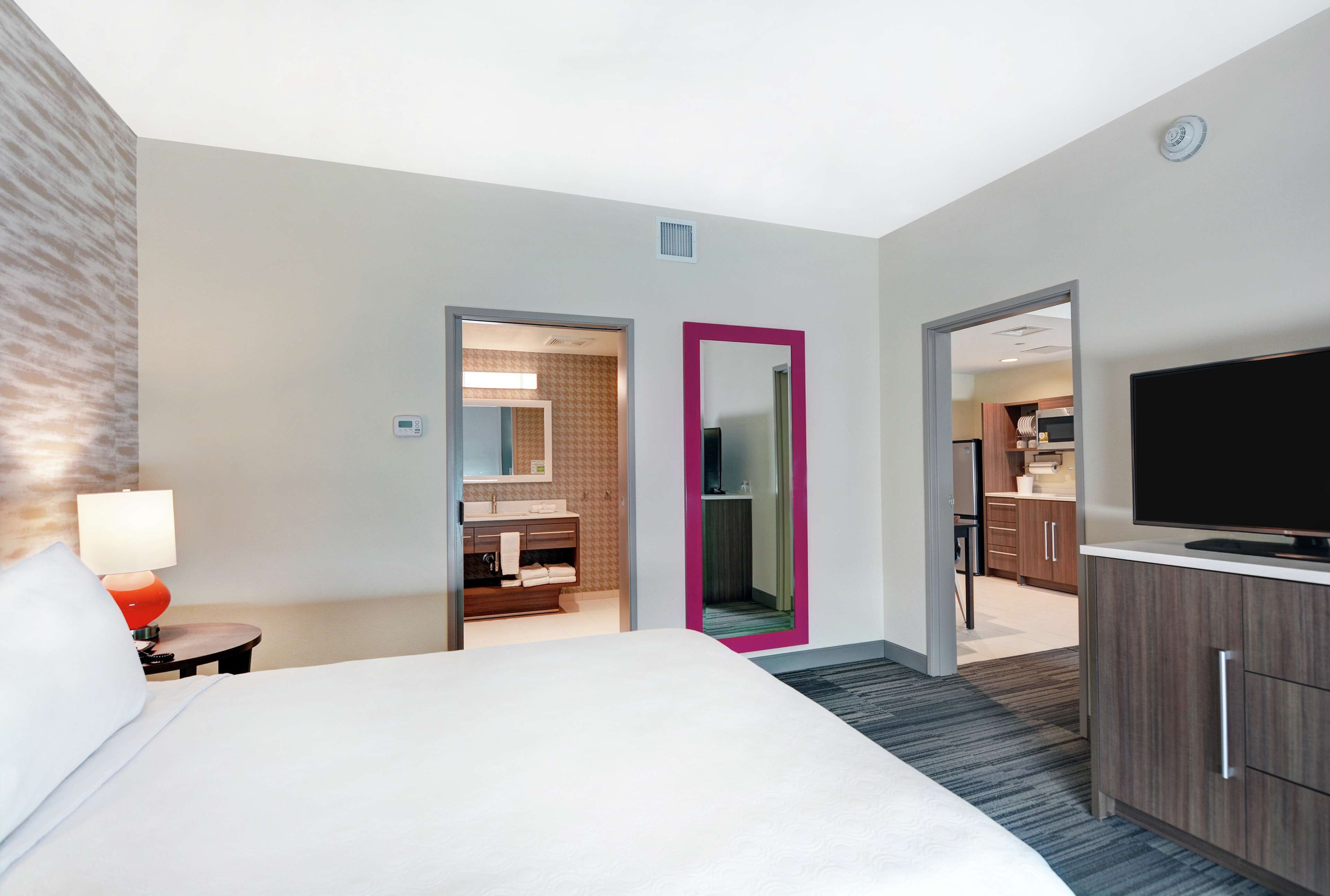 A hotel room with a bed, a TV, a bathroom with a mirror, and a kitchenette.