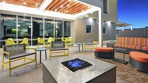 Een terras buiten met gele stoelen, een vuurkorf en een overdekte patio.