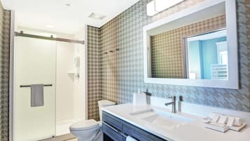 A modern bathroom with a glass shower enclosure, a white toilet, a vanity with a large mirror, and patterned wallpaper.