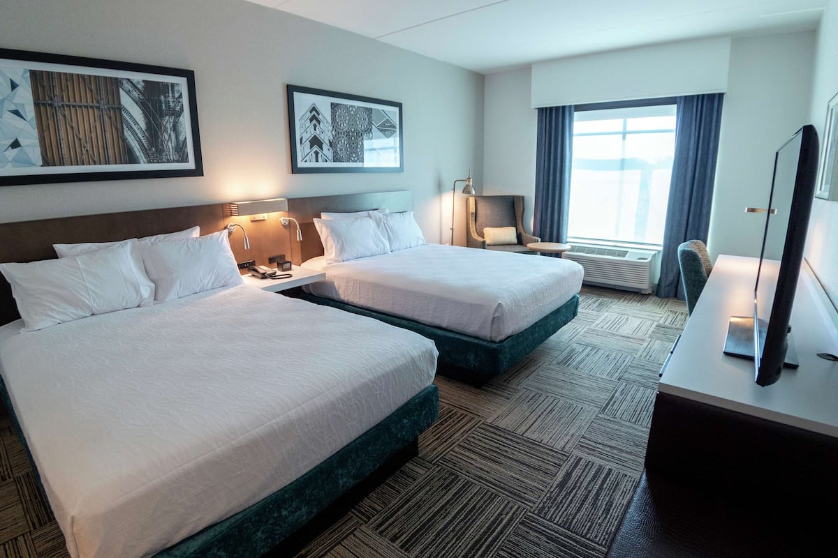 Een hotelkamer met twee bedden, een bureau, een stoel, een televisie en kunstwerken aan de wanden.