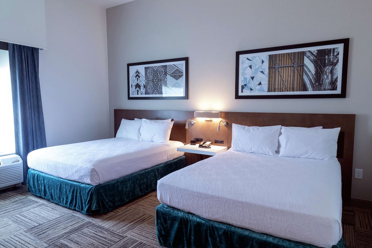 Een hotelkamer met twee bedden, een nachtkastje met een lamp en twee ingelijste foto's aan de muur.