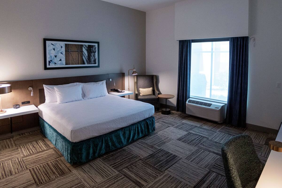Een hotelkamer met een groot bed, een bureau, een stoel, een airconditioning en een raam met gordijnen.