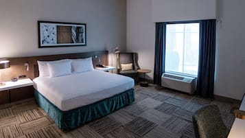 A hotel room with a large bed, a desk, a chair, an air conditioning unit, and a window with curtains.