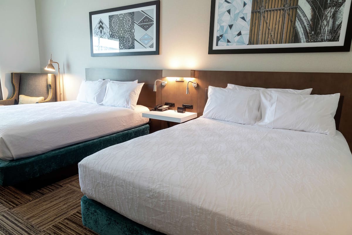 Een hotelkamer met twee bedden, een nachtkastje, een lamp en kunstwerken aan de muur.