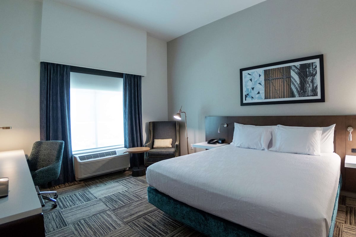 Een hotelkamer met een groot bed, een bureau, een stoel, een bureaulamp, een telefoon aan de muur en een raam met gordijnen.