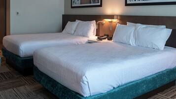 Habitación de hotel con dos camas, cada una con ropa blanca, cabeceros, lámparas de noche y piso alfombrado.