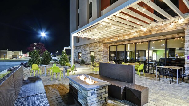 An outdoor patio with stone seating, a fire pit, and string lights. - Home2 Suites by Hilton Warner Robins (Warner Robins)