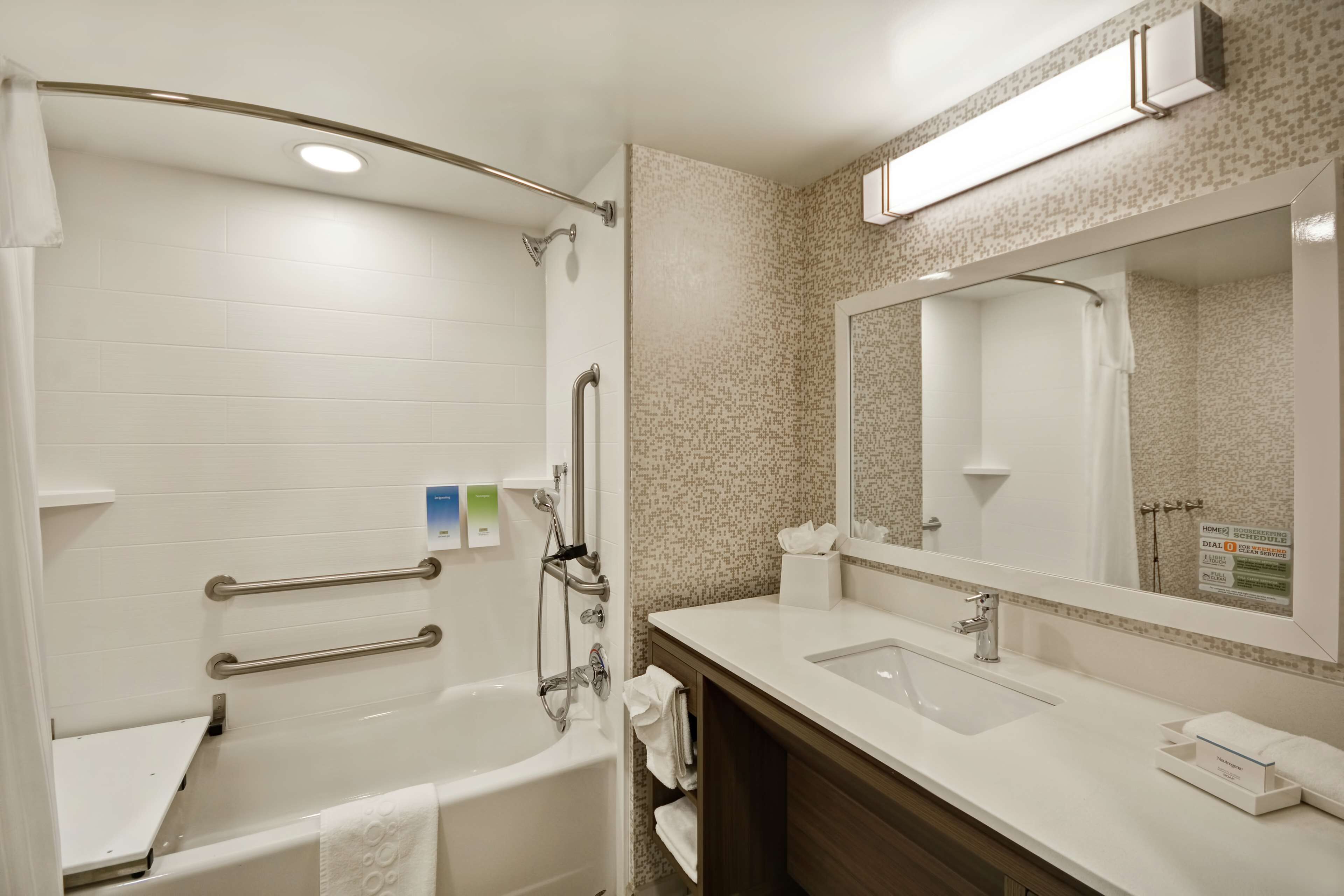 Une salle de bain moderne dotée d’une douche à l’italienne, de barres d’appui, d’un grand miroir et d’un meuble-lavabo avec un évier et un porte-serviettes.