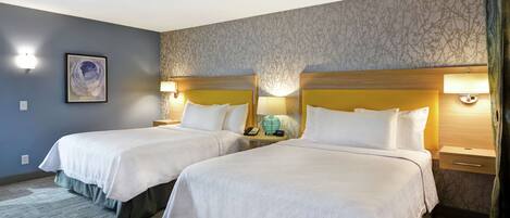 Habitación de hotel con dos camas, cada una con cabecero de madera, ropa de cama blanca y lámparas de noche.