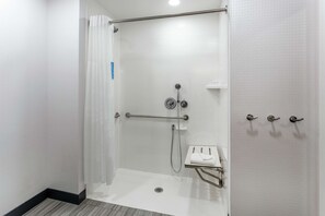 A walk-in shower with a glass door, a handrail, and a small shelf with a towel. - Hampton Inn Oakland Downtown-City Center (Oakland)