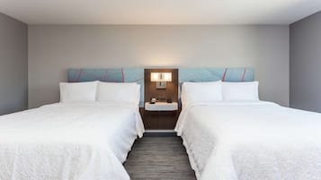 A hotel room with two beds, a nightstand, a wall-mounted lamp, and a small sink.
