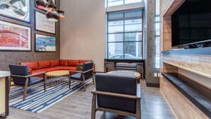 A modern lounge area with a red sectional sofa, a chess table, and a large TV screen. - Hampton Inn Oakland Downtown-City Center (Oakland)