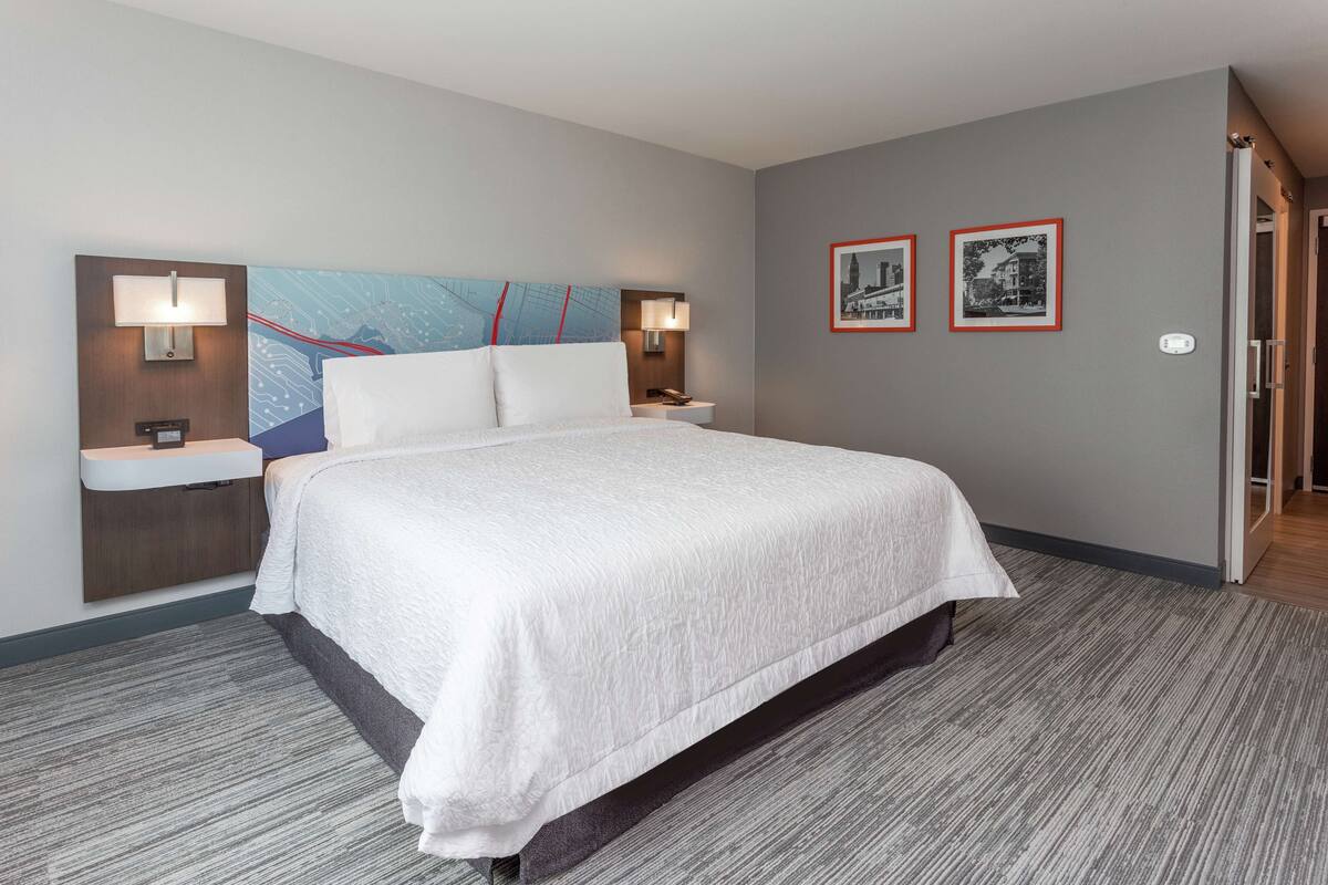 Habitación de hotel con una cama grande, dos mesitas de noche con lámparas, un mapa colgado en la pared y dos cuadros enmarcados.