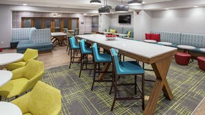 A modern dining area with a long table, blue and yellow chairs, and a patterned carpet. - Hampton Inn Simpsonville (Simpsonville)