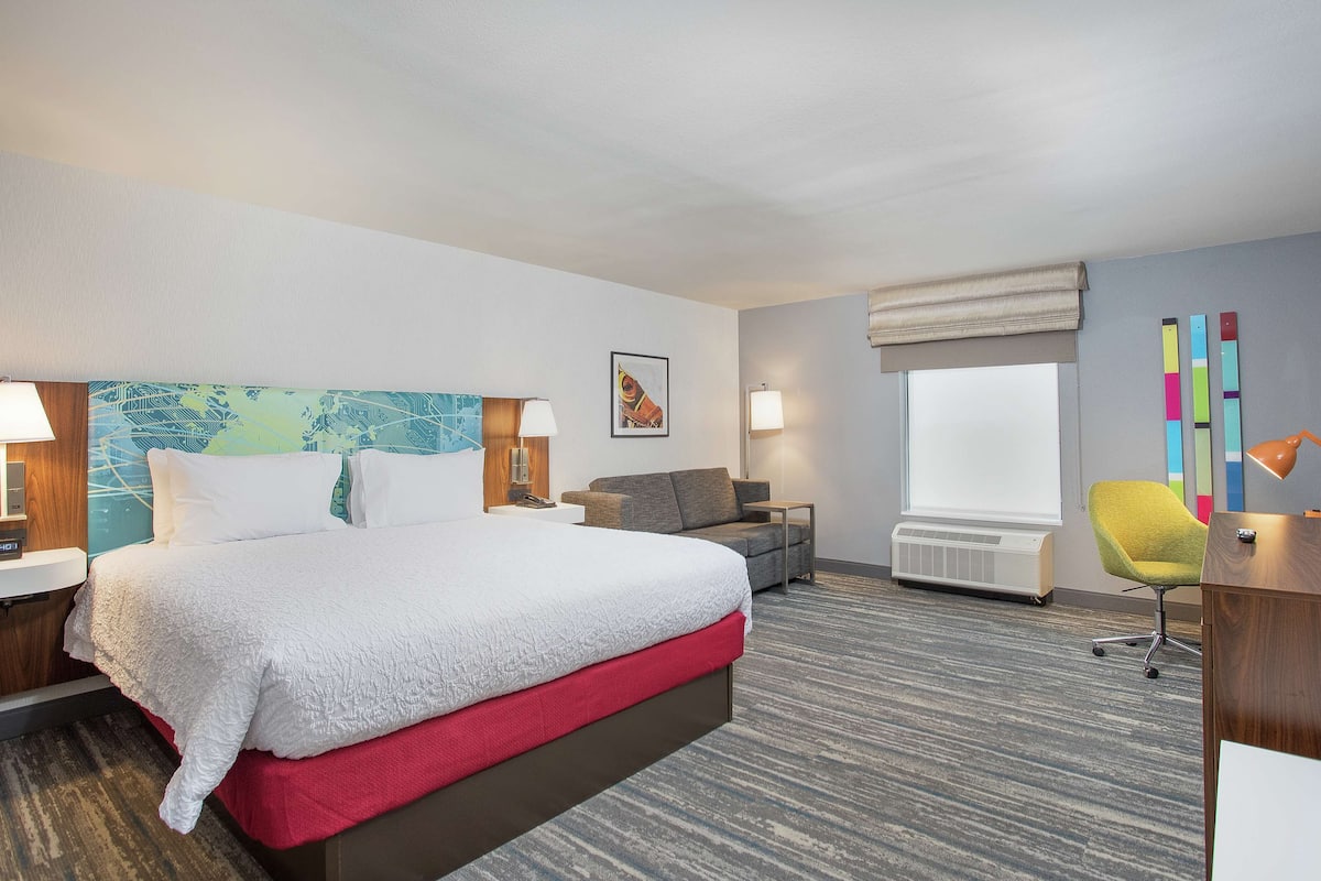 A hotel room with a large bed, a sofa, a desk, and a chair.