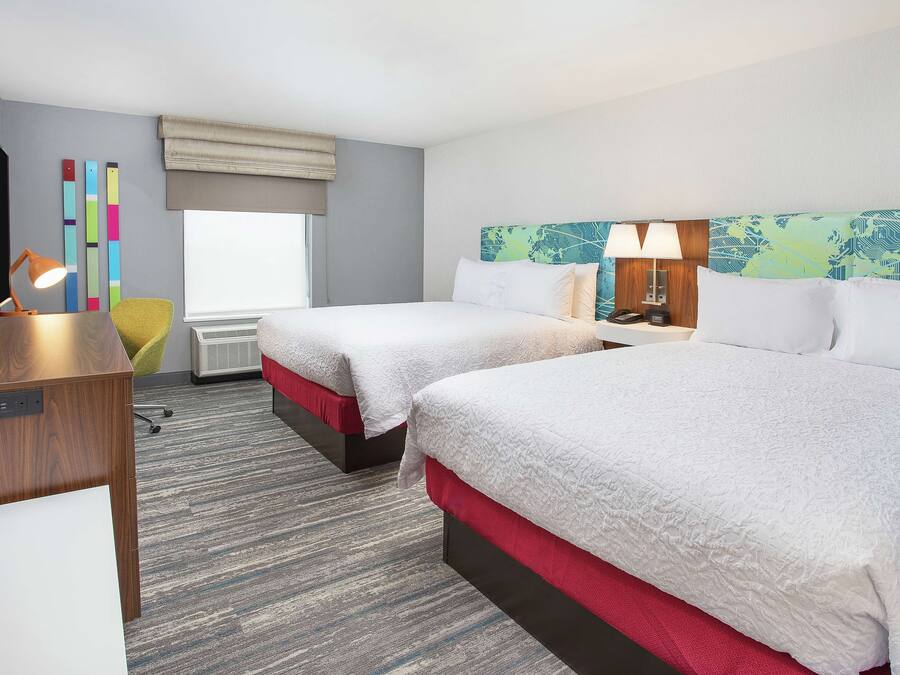 Una habitación de hotel con dos camas, un escritorio, una silla, un televisor y una ventana con vistas.