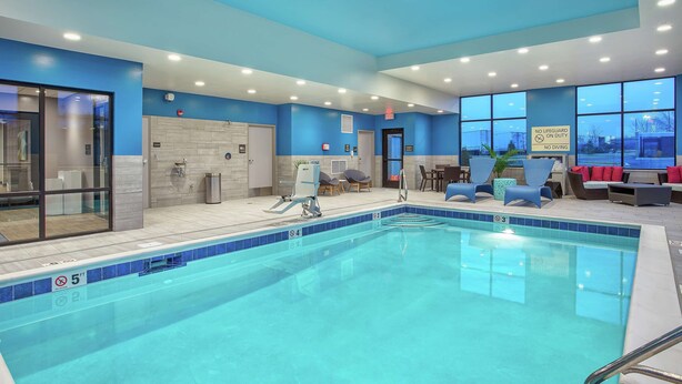 A swimming pool with clear water, surrounded by blue walls and a seating area with chairs and a table. - Hampton Inn Simpsonville (Simpsonville)