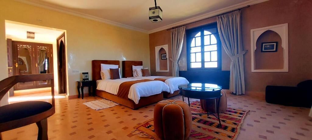 A hotel room with a double bed, a small round table, a chair, and a patterned rug.
