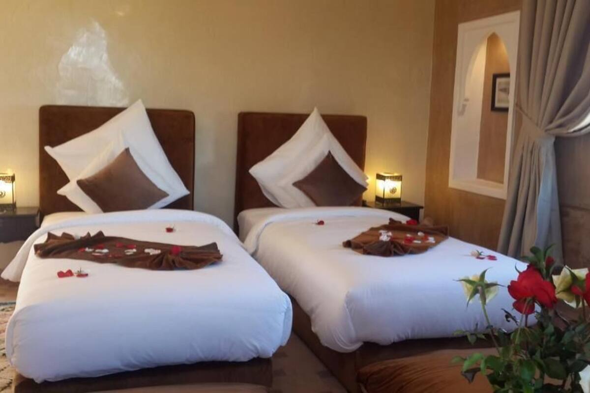 Two single beds with headboards, a nightstand with a lamp, and a window with curtains.