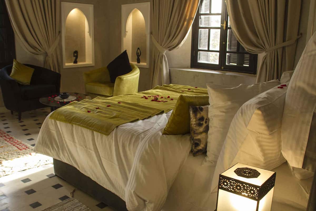 A bedroom with a large bed, two chairs, a small table, and a decorative box.