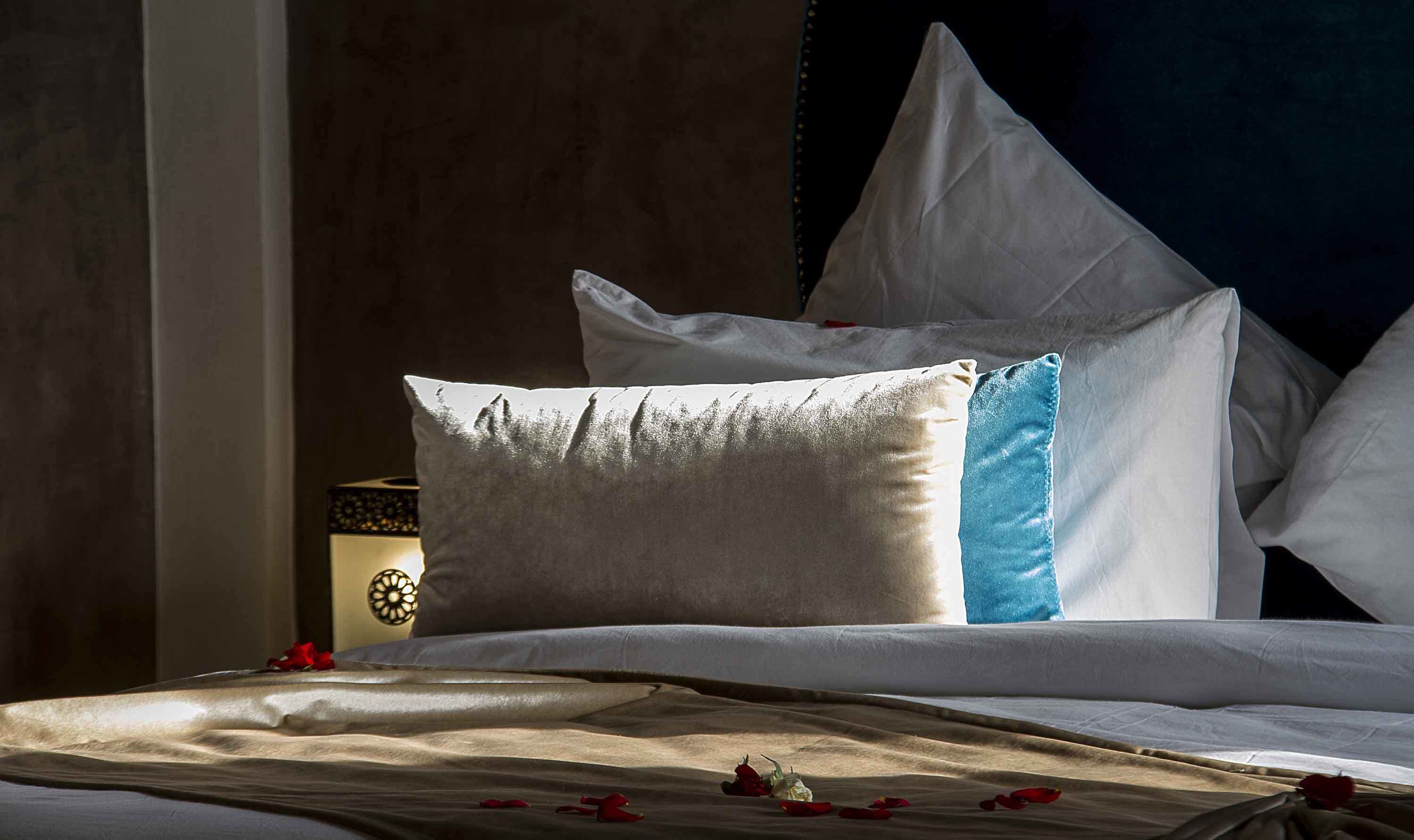 A neatly made bed with white and blue pillows, a decorative wall clock, and scattered rose petals.