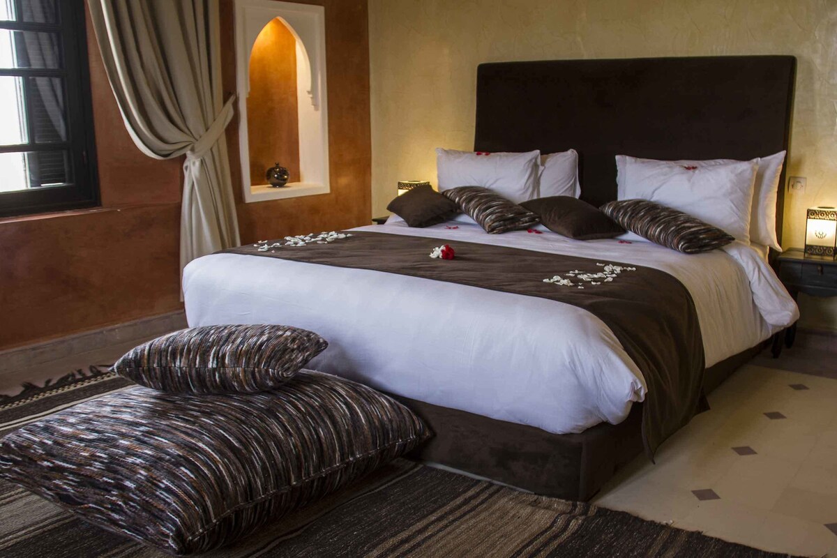 A neatly made bed with a dark headboard, multiple pillows, and a bedside table with a lamp.