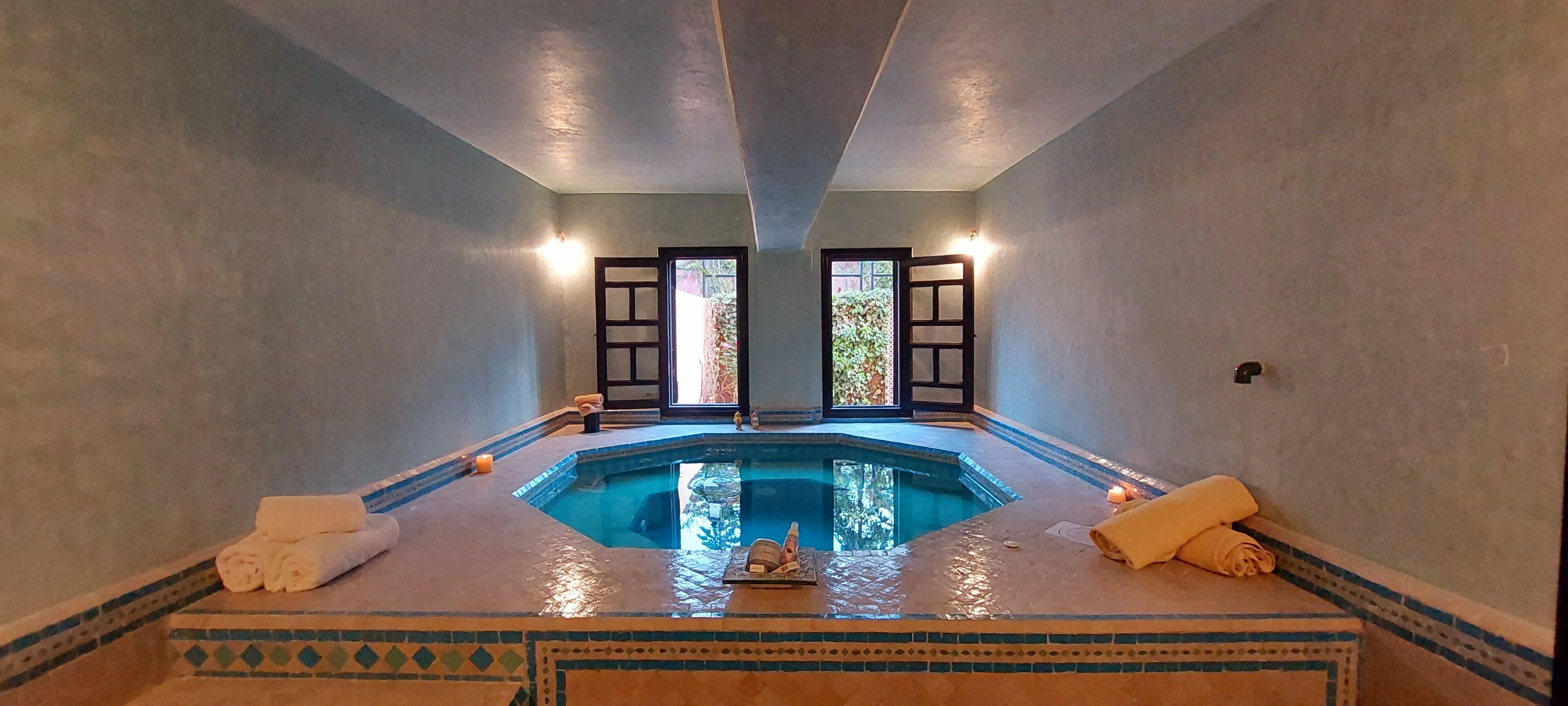 A spa room with a small pool, two open doors leading outside, and towels on the floor.