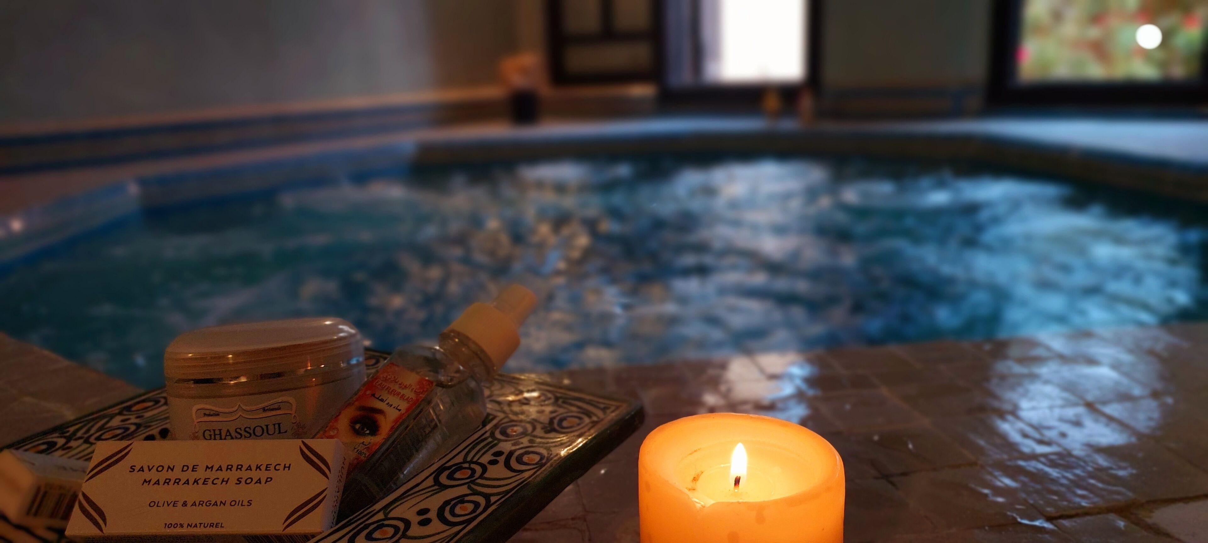 A candle, a jar of soap, and a bottle on a tray by a pool.