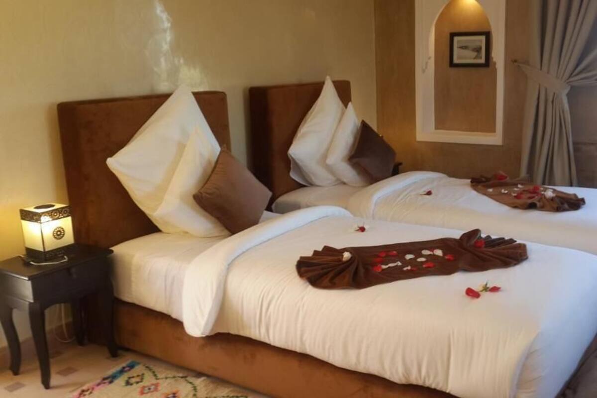 A hotel room with two beds, a nightstand with a lamp, and a framed picture on the wall.