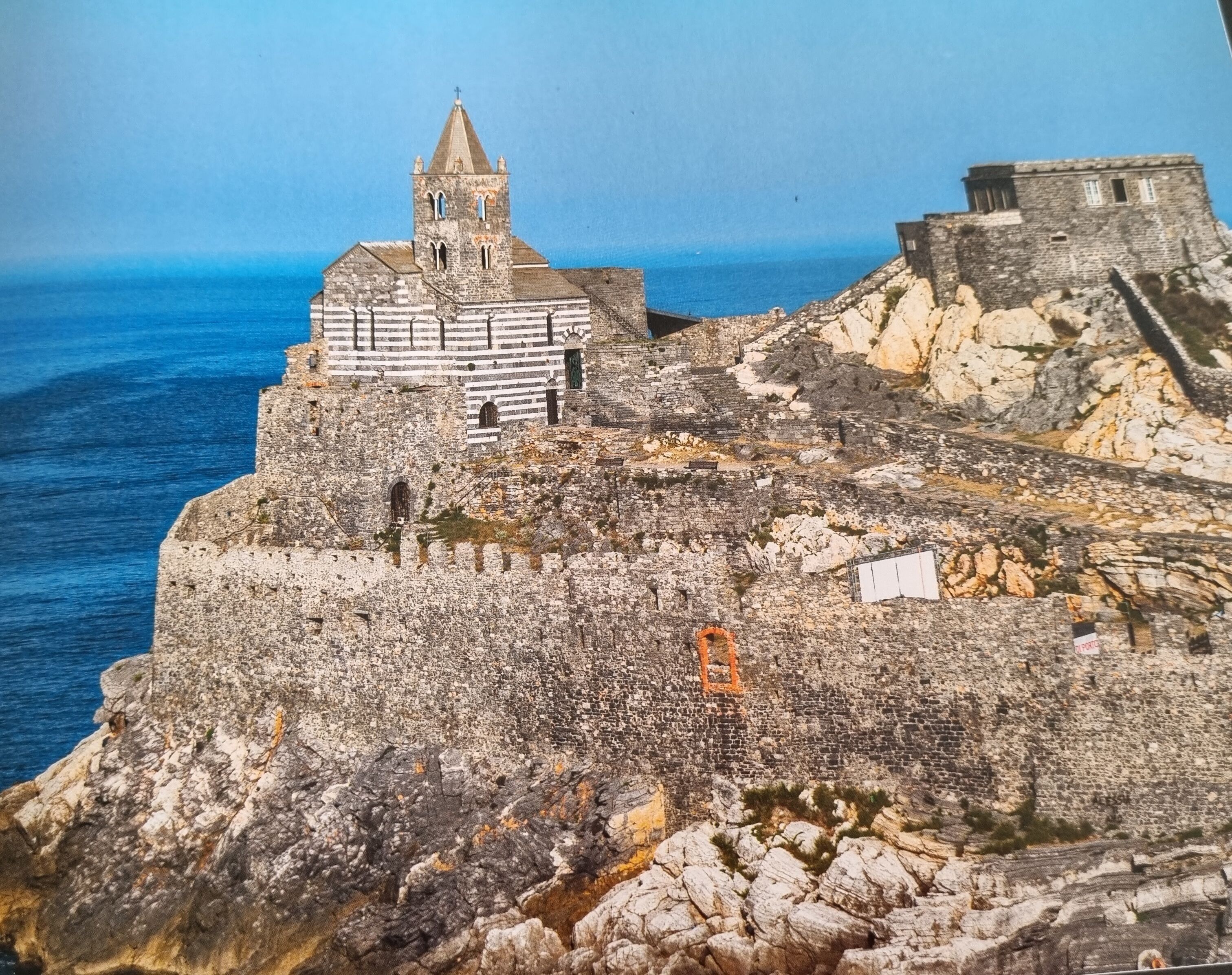 A historic stone building with a tower, situated on a rocky cliff overlooking the sea.