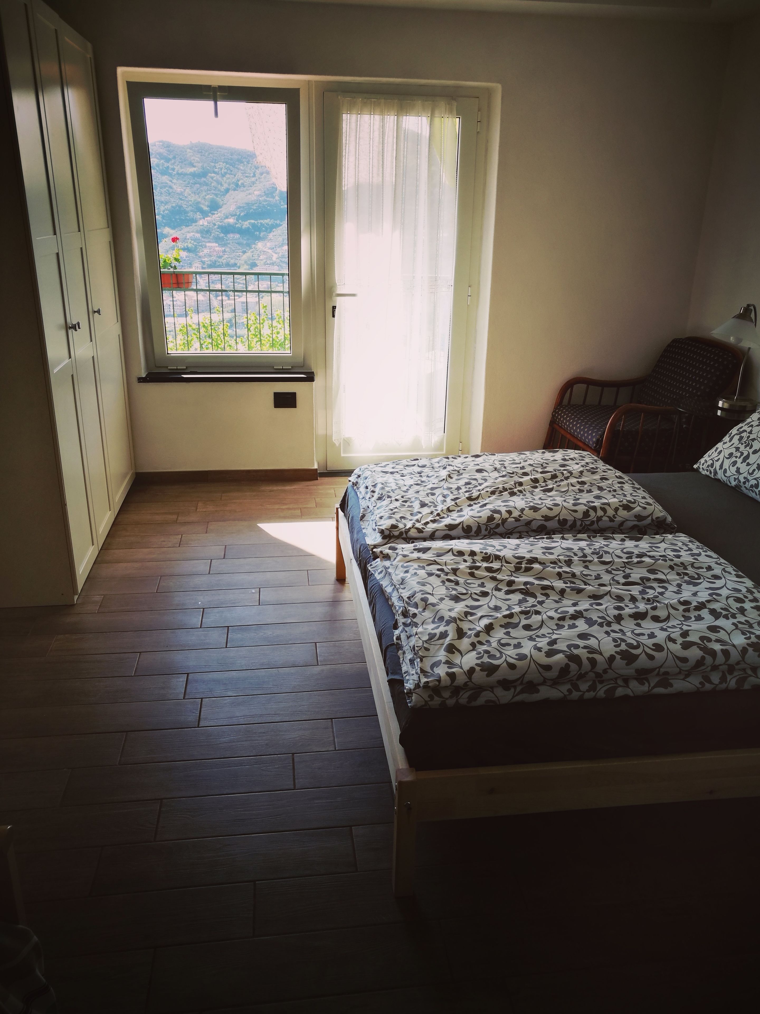 A bedroom with a bed, a chair, a window with a view of greenery, and a wardrobe.