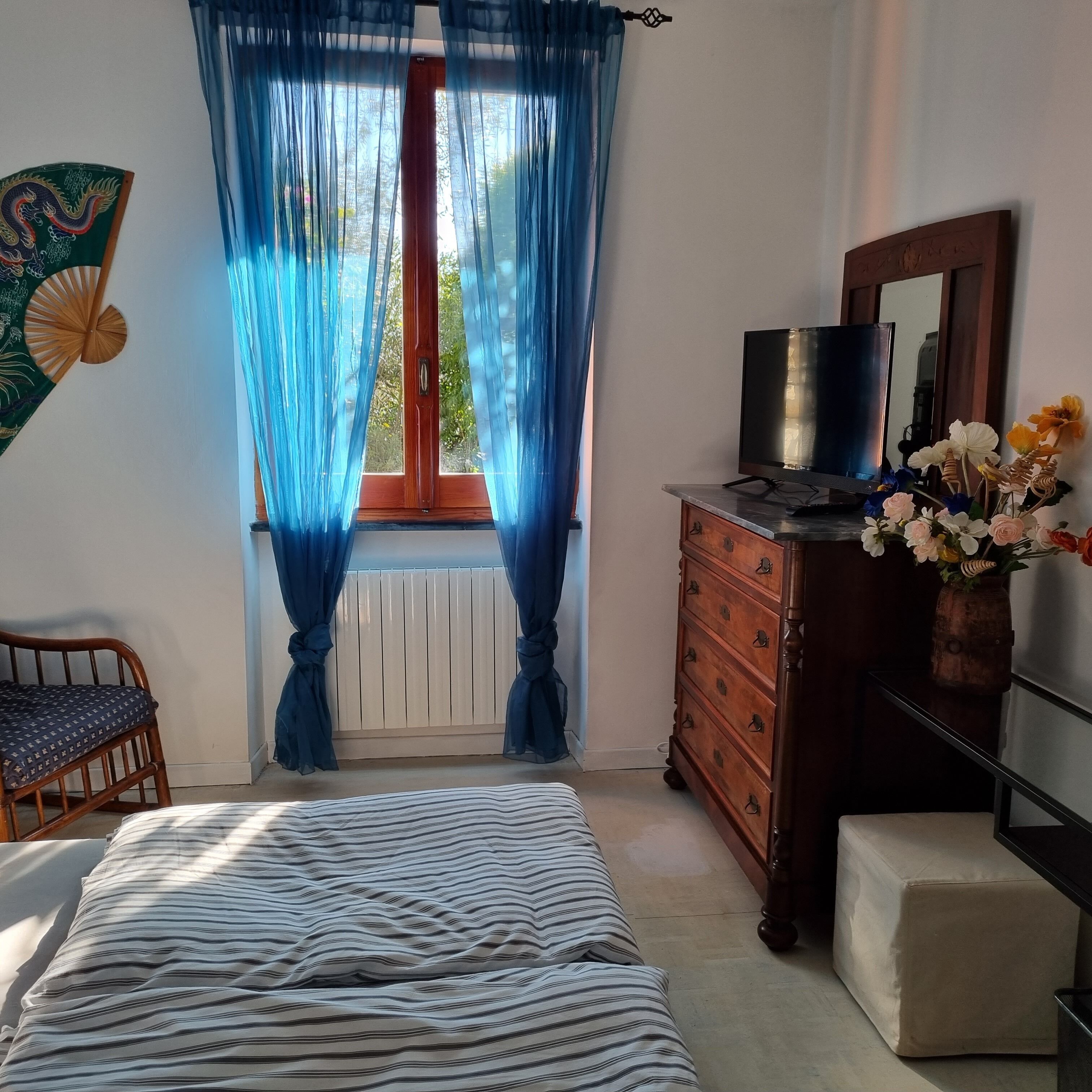 Une chambre à coucher avec un lit, une commode, un téléviseur et une fenêtre avec des rideaux bleus.
