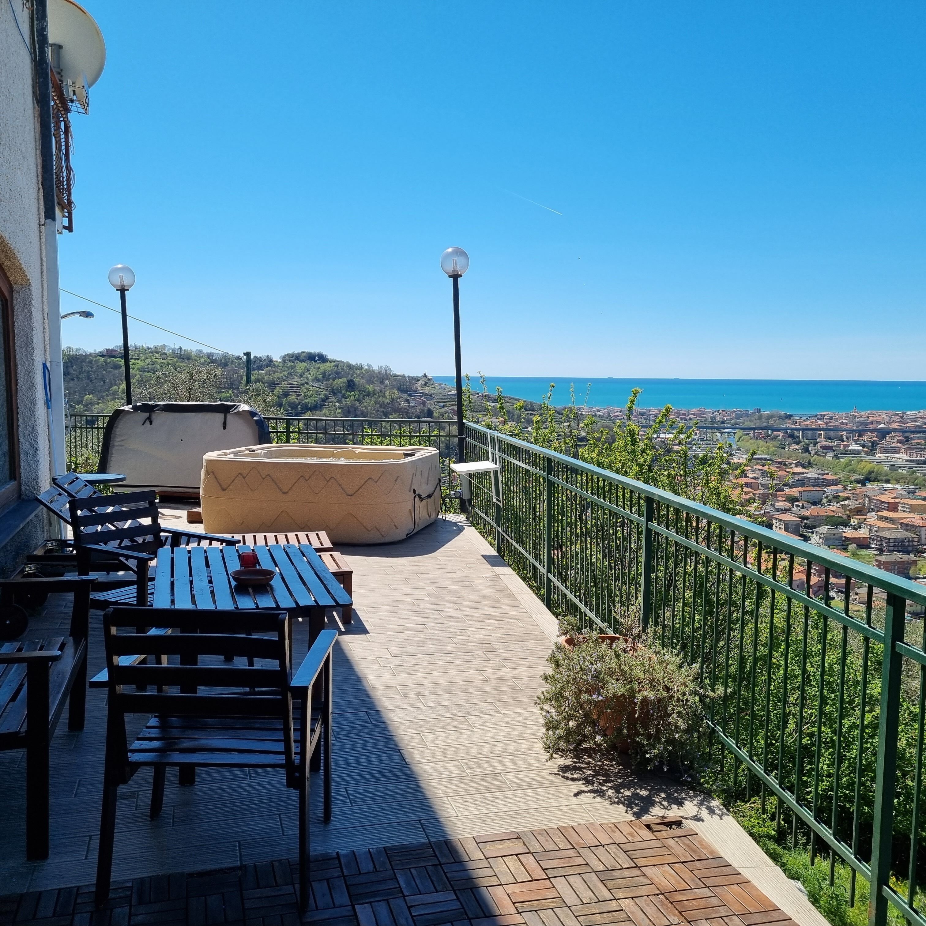 An outdoor terrace with a table and chairs, a cushioned seating area, and a view of a coastal cityscape.