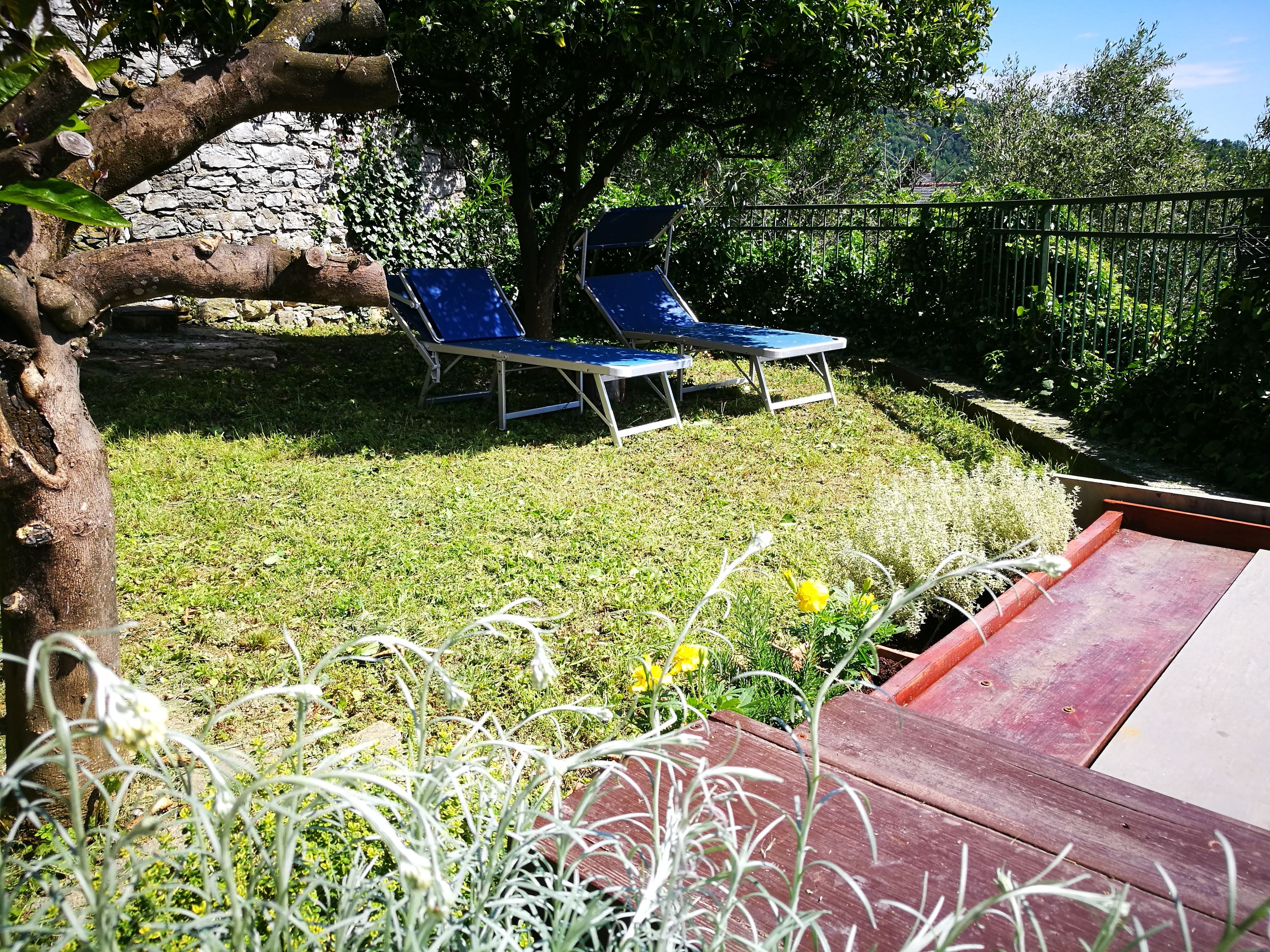 Un jardín con un muro de piedra, dos sillones azules y una terraza de madera.