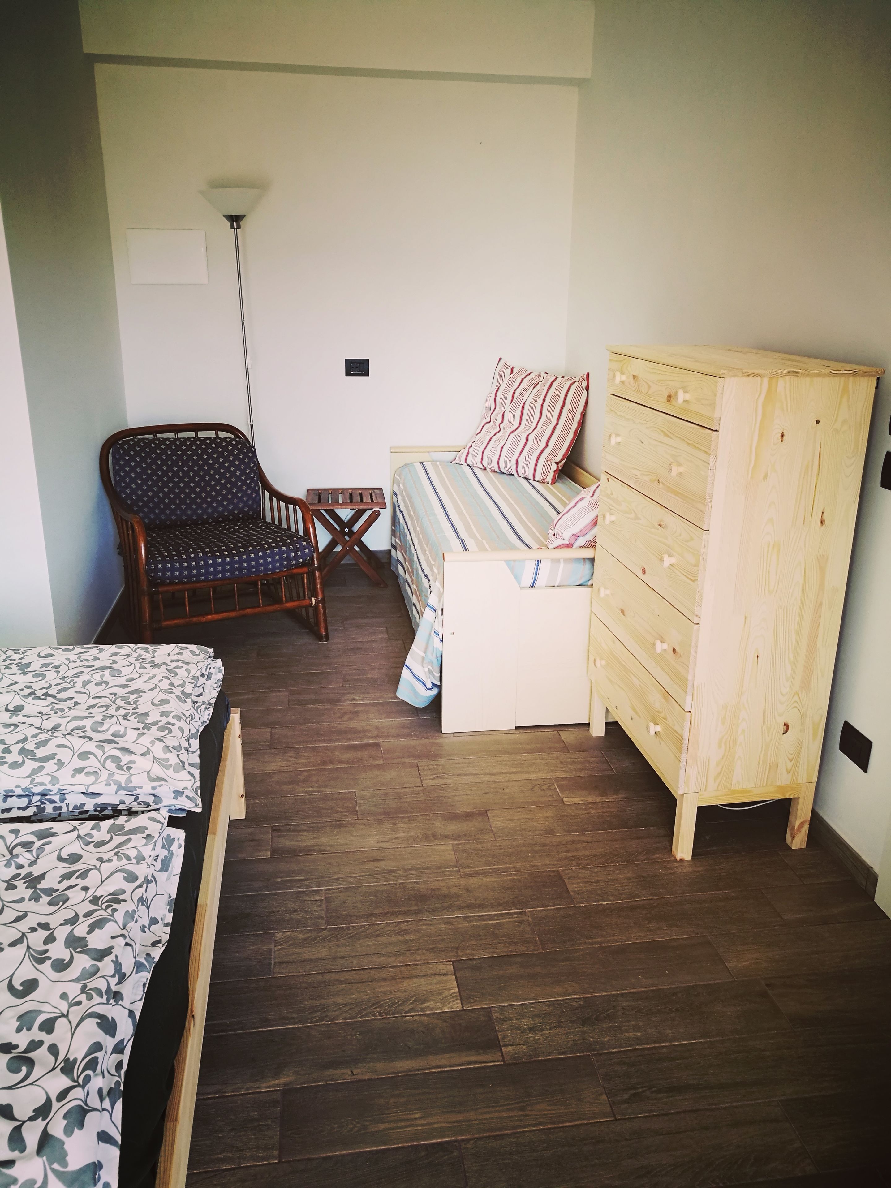 A bedroom with a wooden floor, a bed with striped bedding, a wooden dresser, a chair, and a small table.
