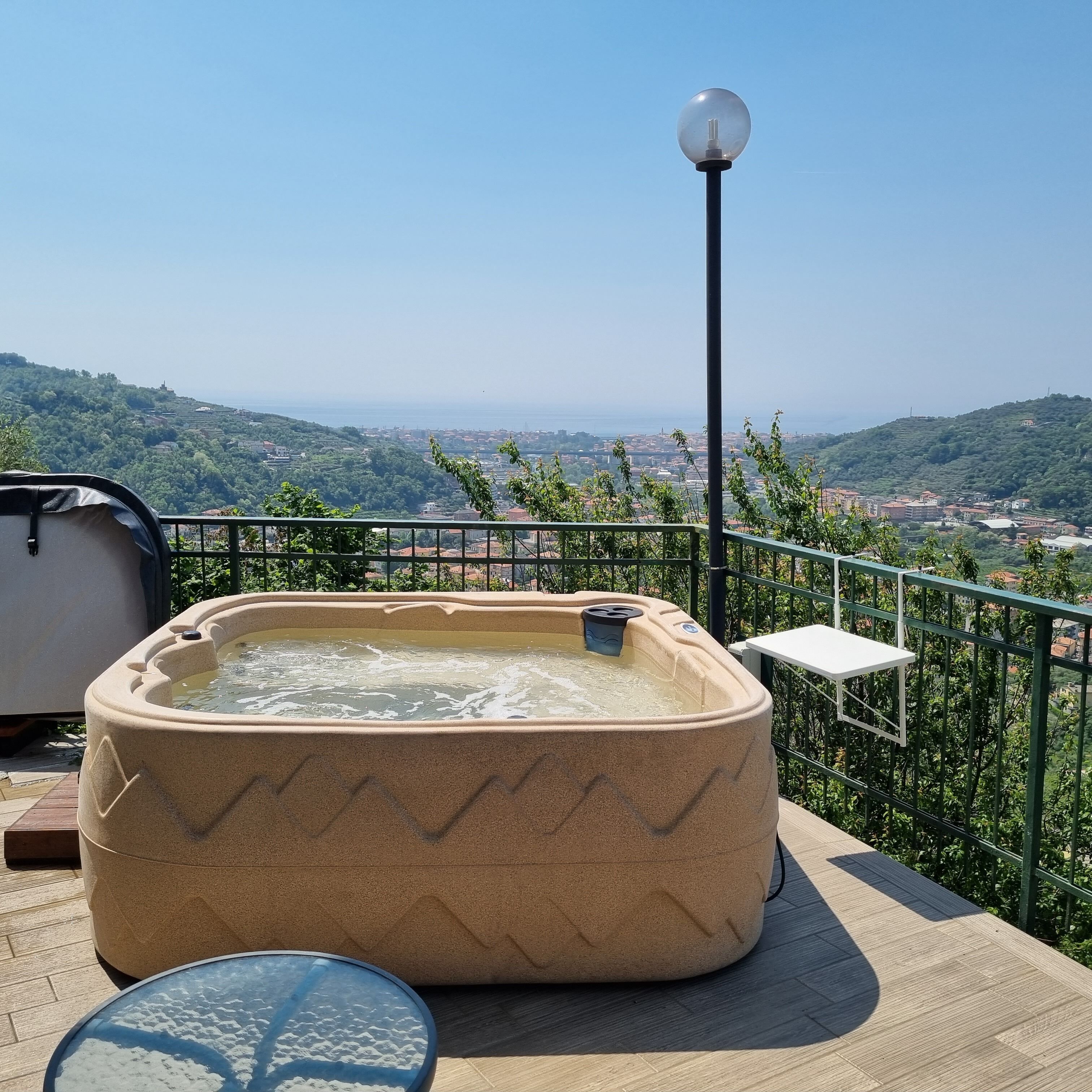 Un jacuzzi en una terraza con vistas despejadas a un paisaje urbano y colinas al fondo.