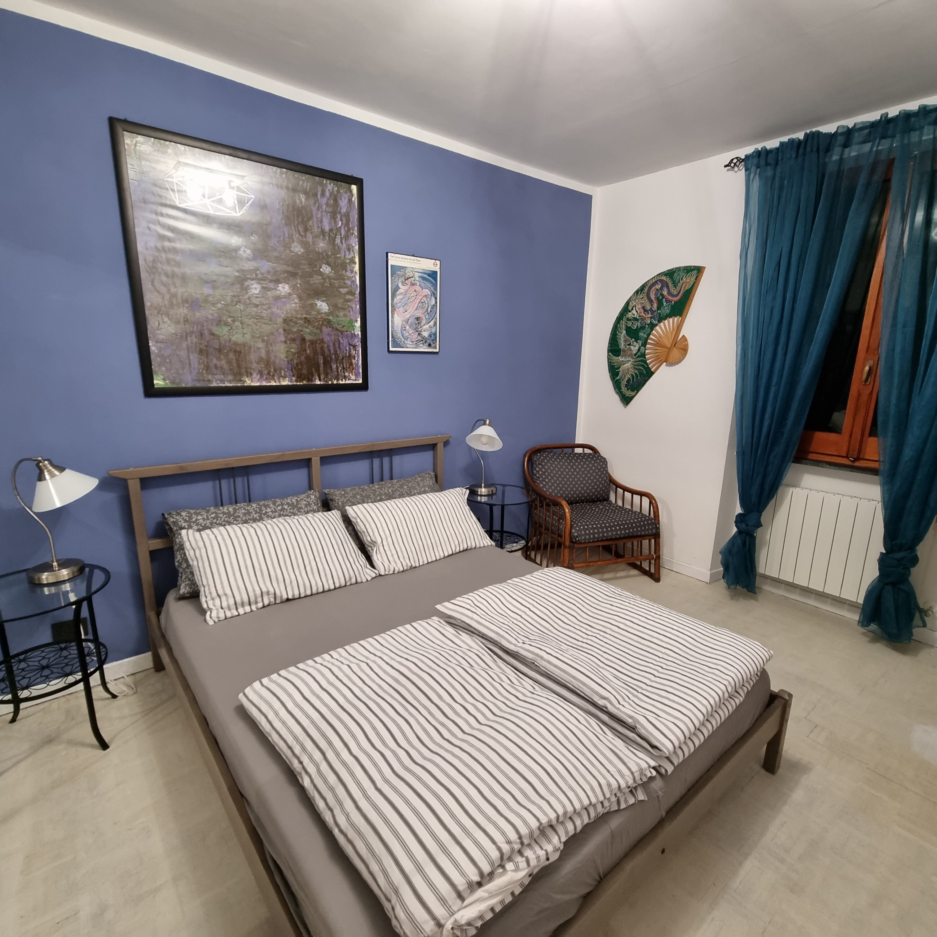 A bedroom with a large bed, a chair, a lamp, and artwork on the walls.