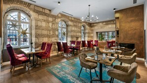 A spacious dining area with high wooden tables and plush red chairs, large arched windows with star decorations, and a modern chandelier. - Monastery Boutique Hotel Budapest (Budapest)
