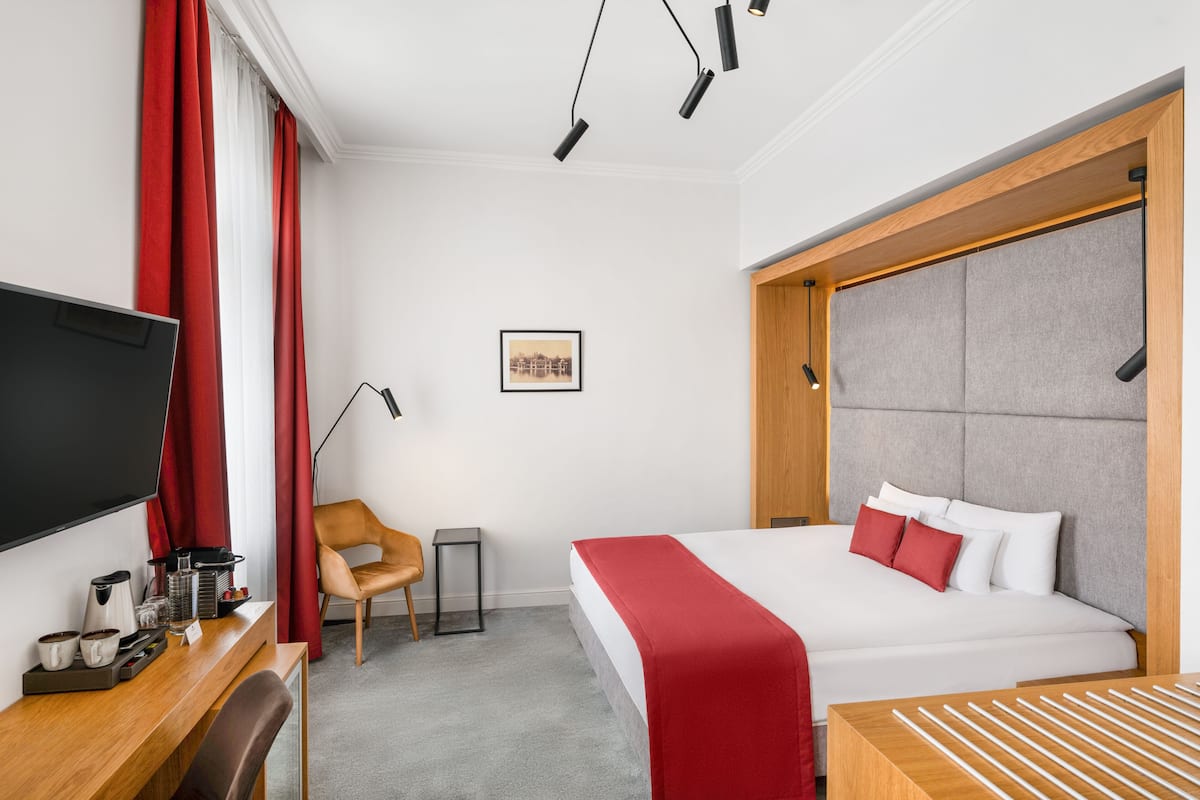 A hotel room with a bed, a desk with a coffee maker, a chair, and a TV.