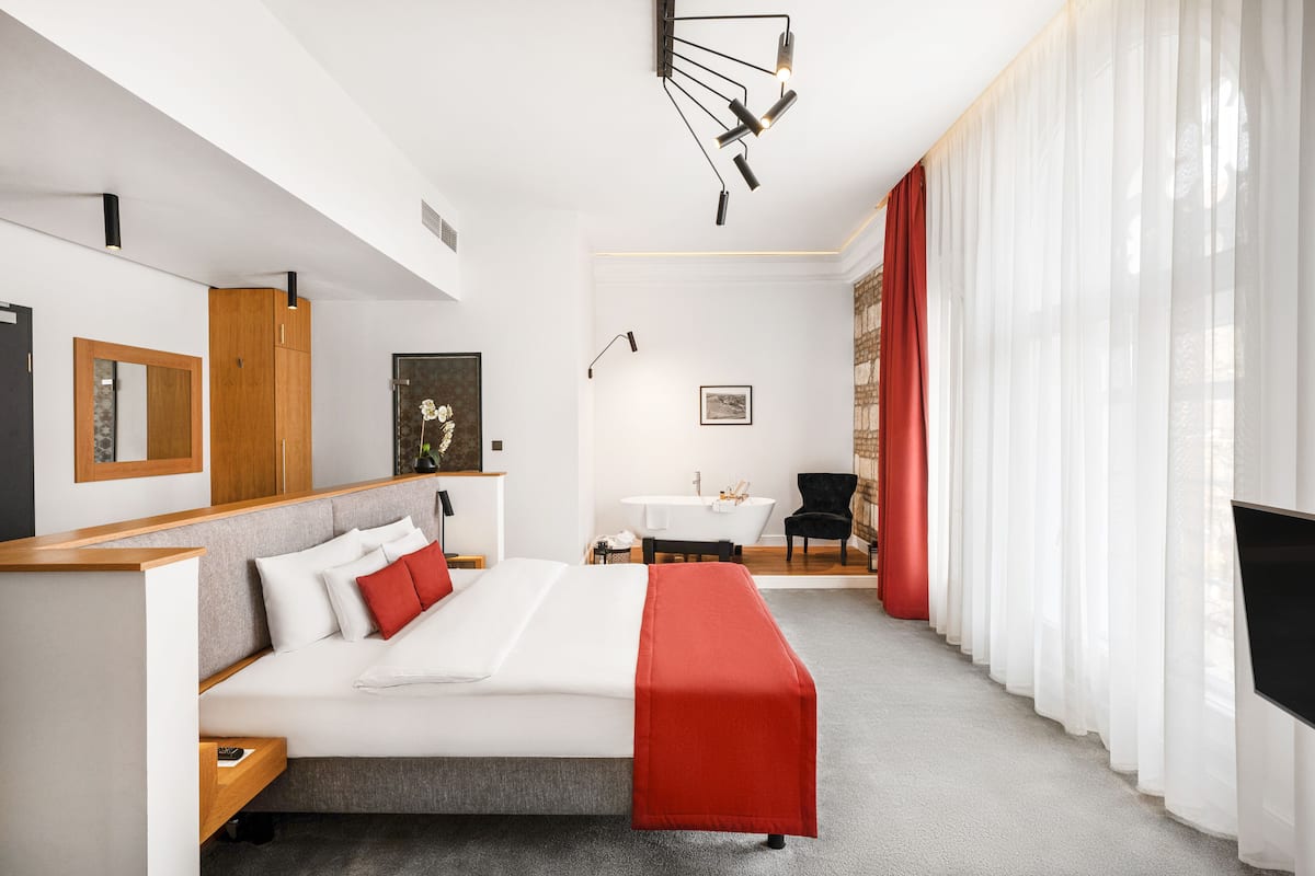 A modern hotel room with a bed, a desk, a chair, and a bathroom.