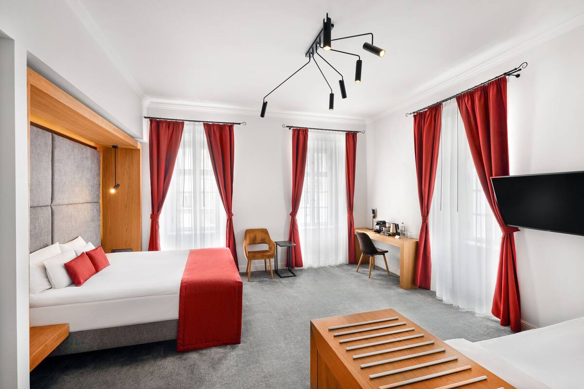A hotel room with a bed, a desk, a chair, a TV, and a ceiling light fixture.