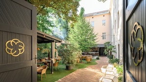Een terras buiten met bakstenen vloer, planten in potten en rieten meubels.