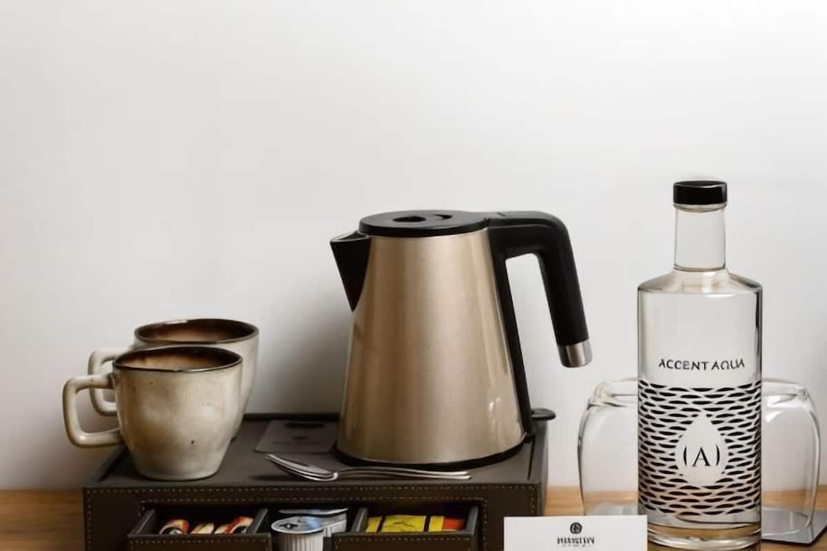 A coffee maker, two mugs, a glass bottle labeled 'Accent Aqua,' and a box of tea bags on a wooden surface.