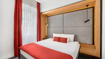 Una camera d'albergo con un letto, tende rosse, una testiera in legno e un lampadario.