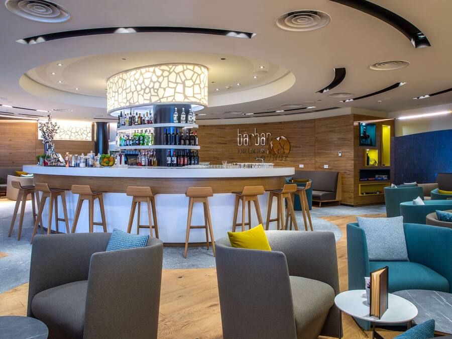 A modern bar area with a central bar, multiple stools, and a variety of seating options including sofas and chairs.