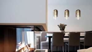 Una sala de estar moderna con una chimenea de vidrio, un comedor con mesa y sillas, y lámparas colgantes sobre la mesa.