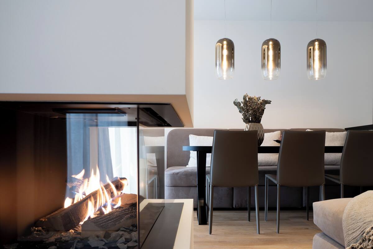 A modern living room with a glass fireplace, a dining area with a table and chairs, and pendant lights above the table.